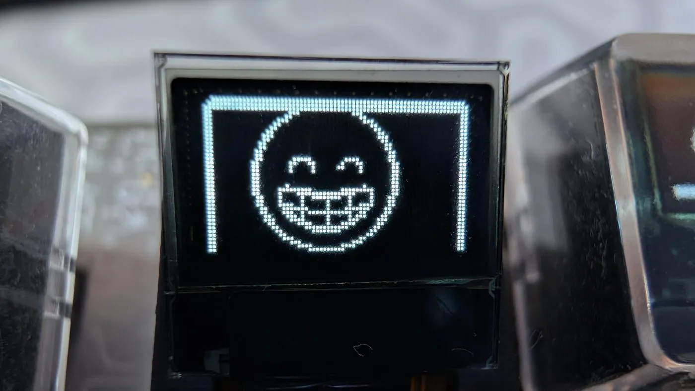 A single keycap OLED rendering a grinning-face emoji at full size