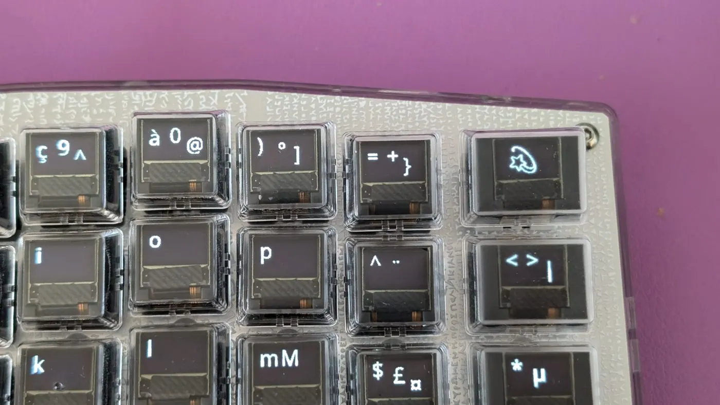 Keycap OLEDs showing a Latin layout with its AltGr symbols: Γ§, Γ , β¬, Β΅, and the bracket and slash keys